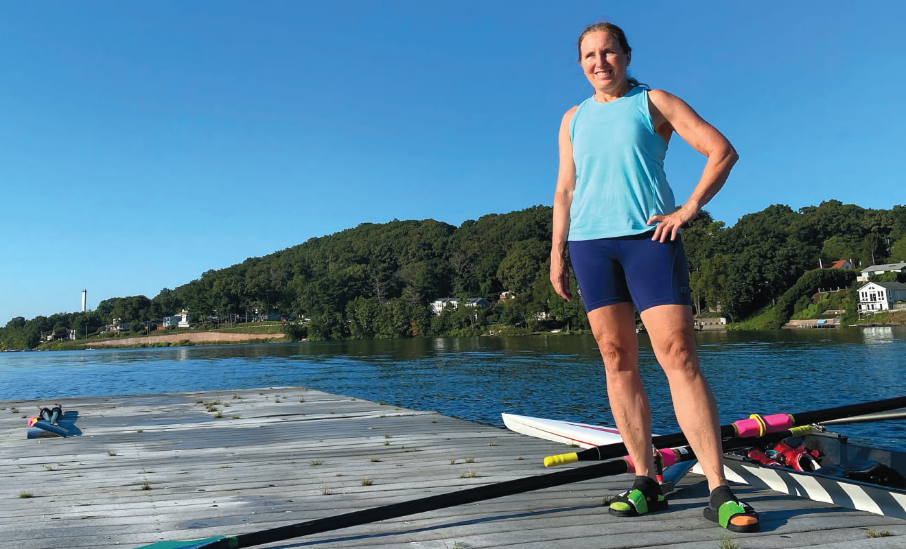 Carla Ferrara ’83 standing on a dock with a crew shell and oar behind her
