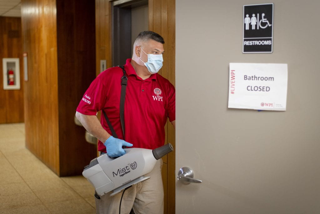A Facilities employee enters a bathroom with a fogging device