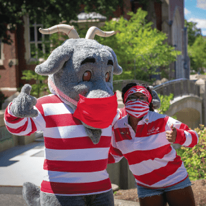 the Gompei the Goat mascot with its arm around a student; both wear red-and-white striped shirts