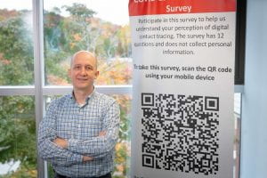 Patrick Schaumont stands next to a poster with information about a survey and a large QR code