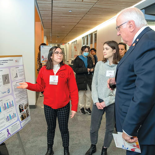 A student in a red jacket explains her research poster to donors